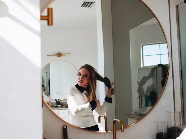 Woman brushing her hair in a bathroom with a round mirror
