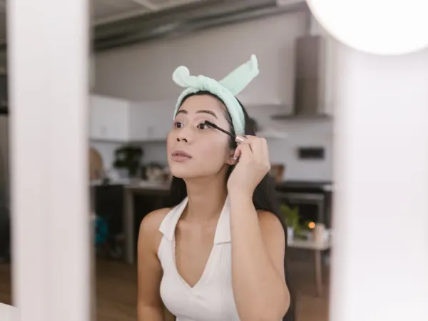 A woman using makeup tools at her mirror
