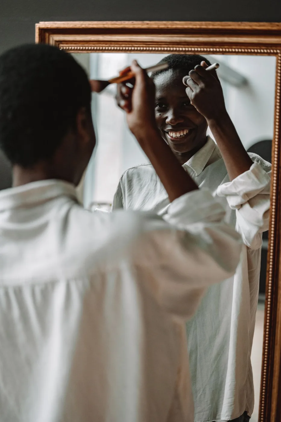 Woman smiling while applying makeup at a mirror